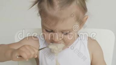 一个小女孩坐在孩子们`桌子旁，用勺子吃粥